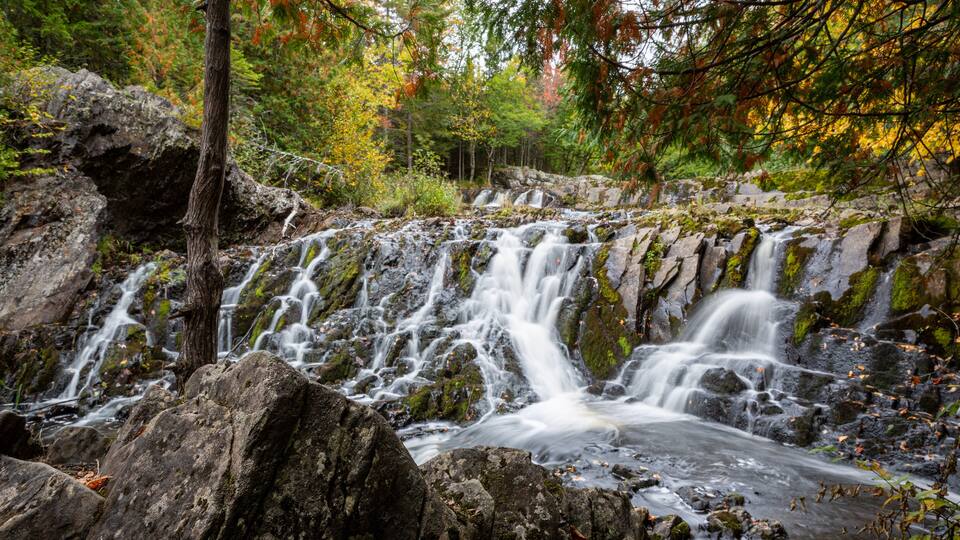 A waterfall cascading over rocks in a forested area with autumn foliage.