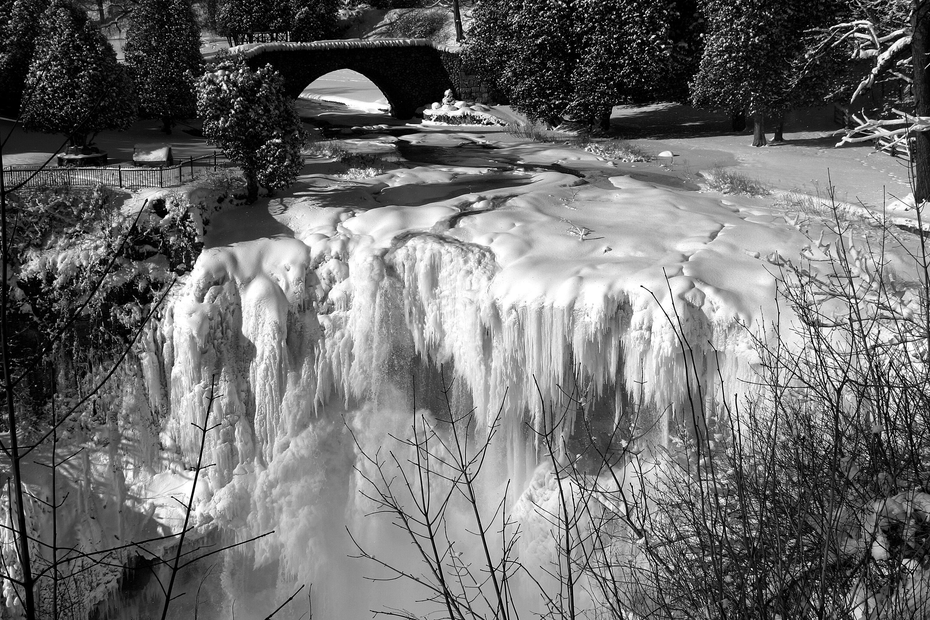 A frozen waterfall, a stone bridge, and snow-covered trees.