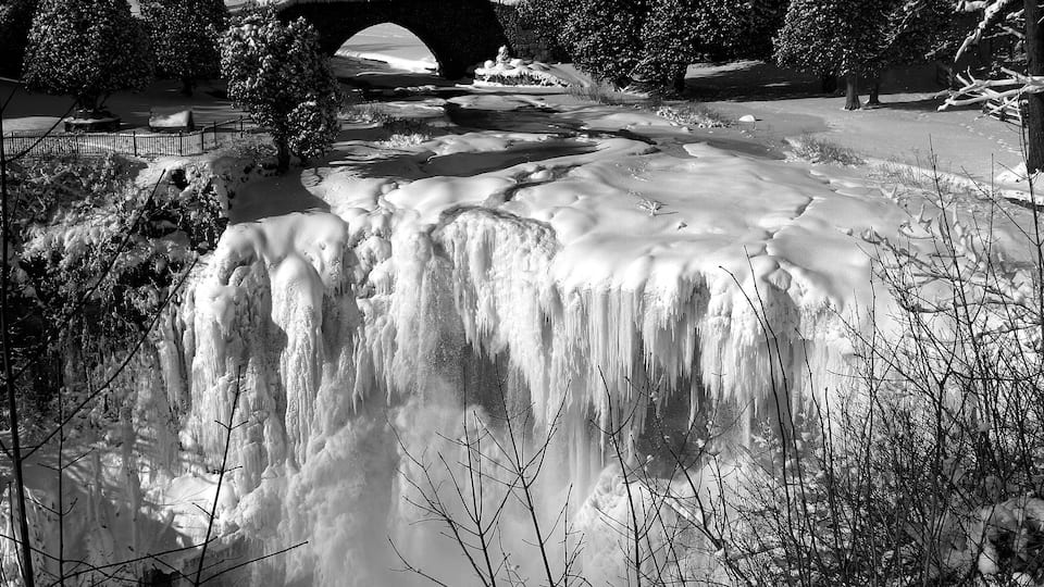A frozen waterfall, a stone bridge, and snow-covered trees.