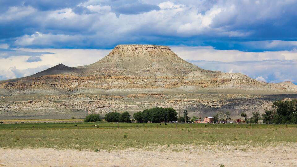 A mountain with a flat top, surrounded by a grassy field and a few scattered trees.