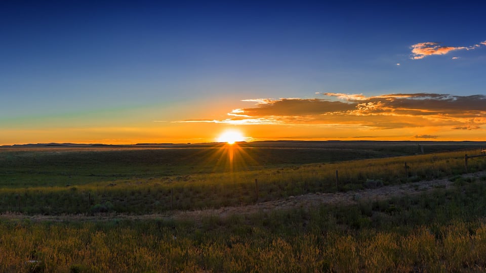 A sunset over a grassy field with a fence in the foreground.