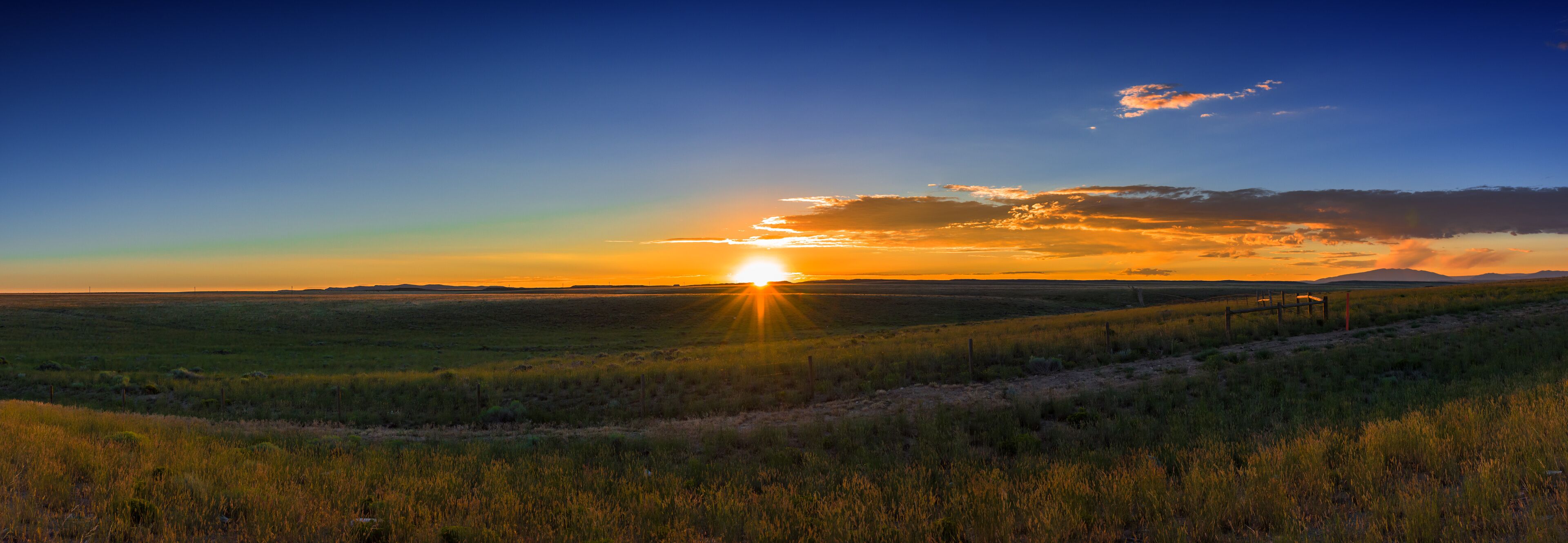 A sunset over a grassy field with a fence in the foreground.