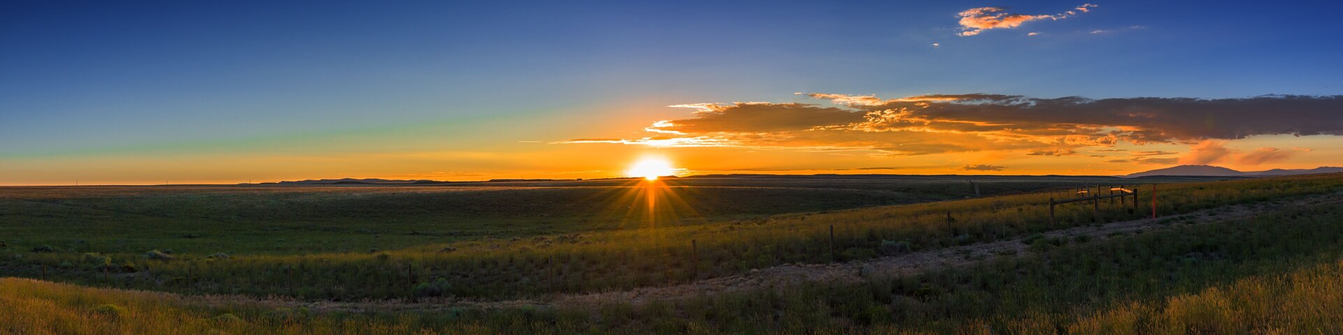 A sunset over a grassy field with a fence in the foreground.
