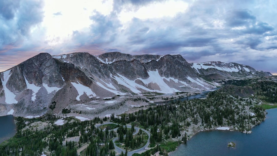 A mountain range with snow patches, two lakes, and a winding road.