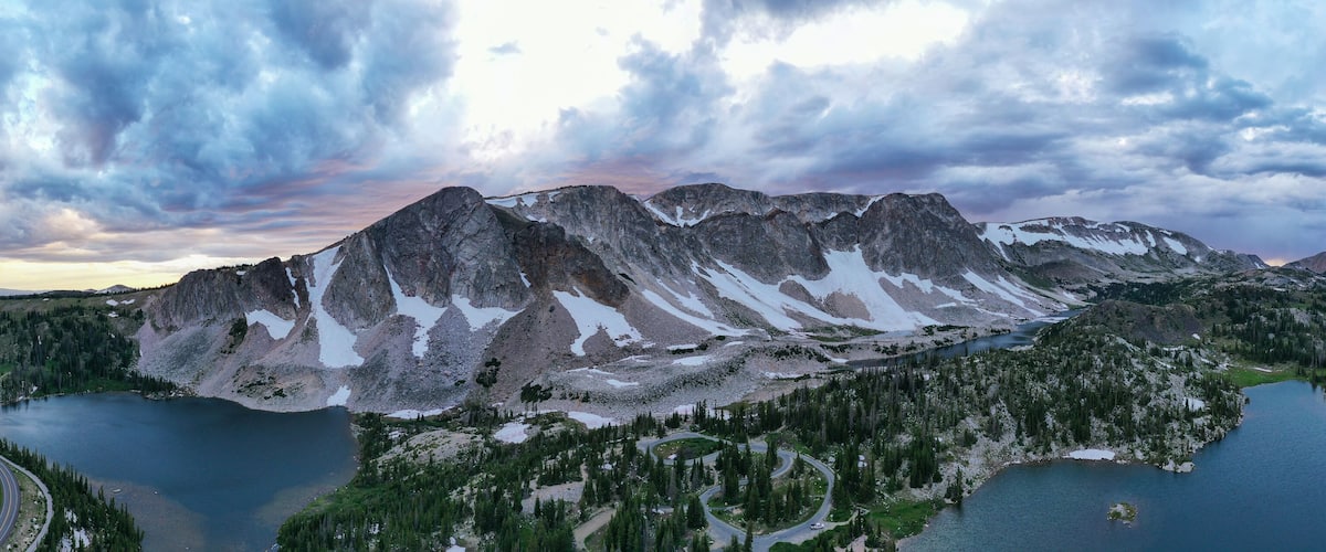 A mountain range with snow patches, two lakes, and a winding road.