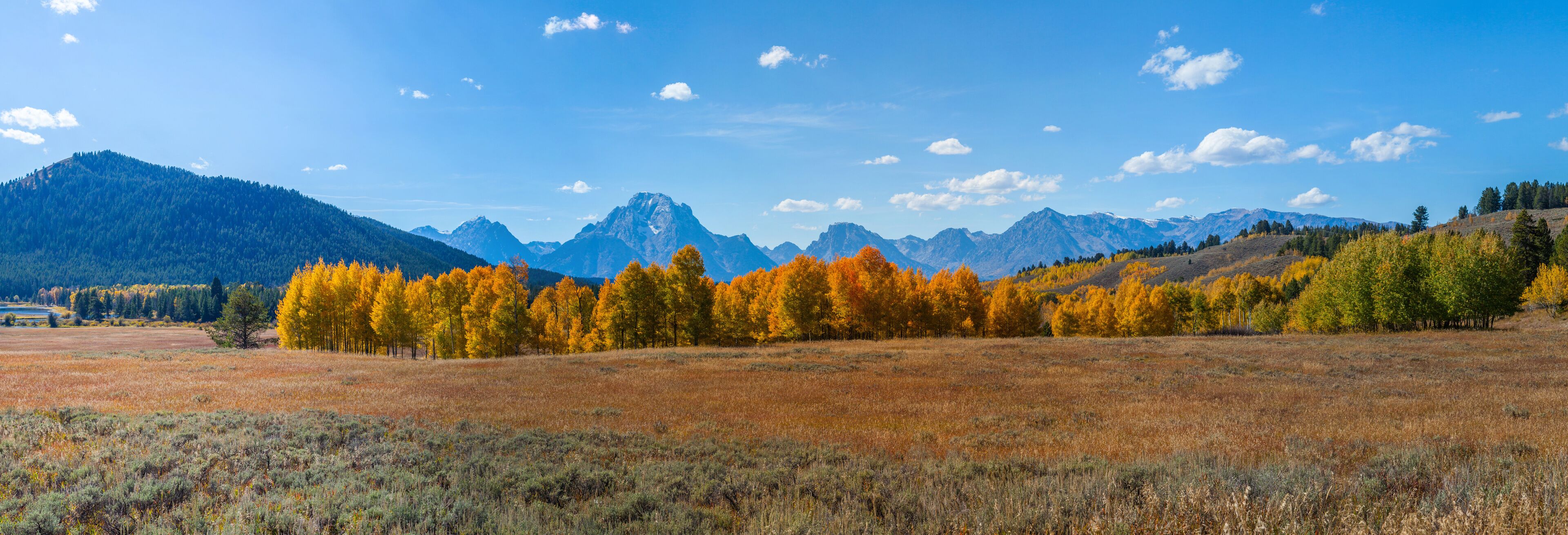 A mountainous landscape with autumn-colored trees and a clear blue sky.