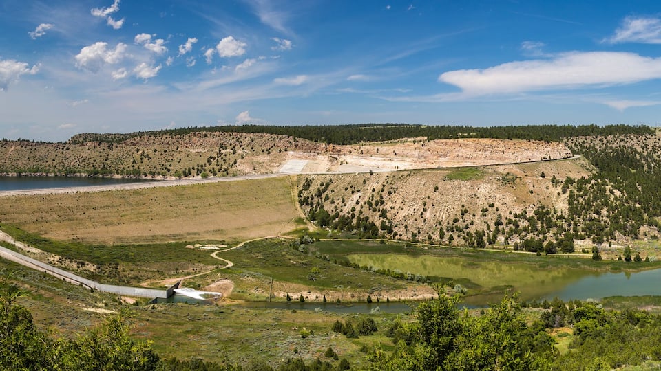 A dam, reservoir, and surrounding landscape with hills and trees.