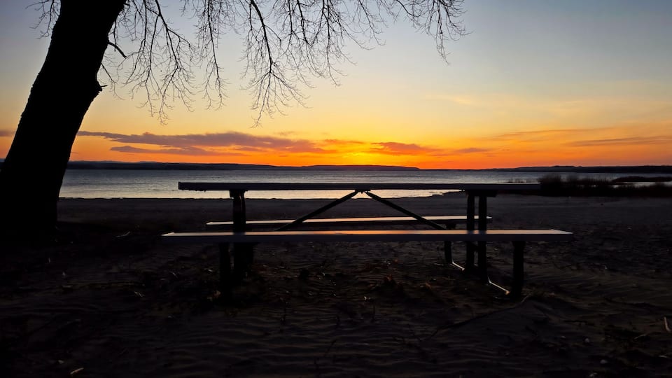 A beach with a picnic table and a sunset in the background.