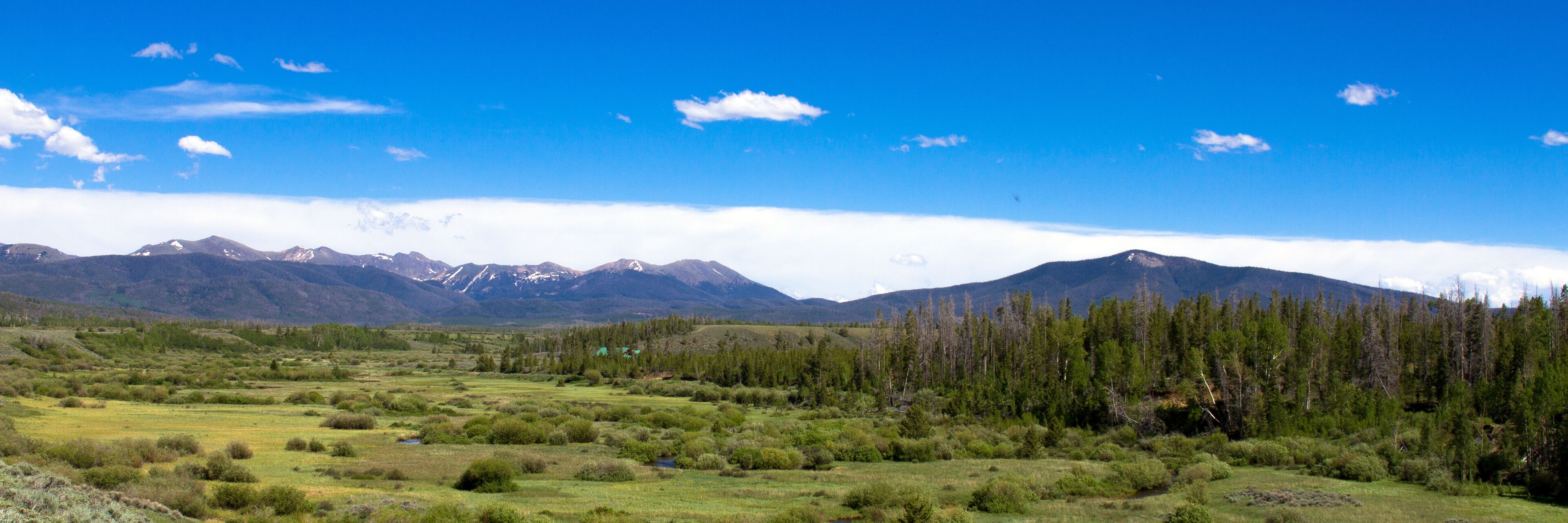 A mountainous landscape with a clear sky, a river, and a forested area.
