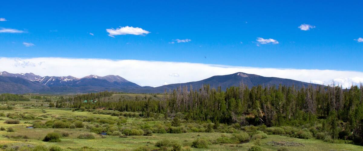 A mountainous landscape with a clear sky, a river, and a forested area.