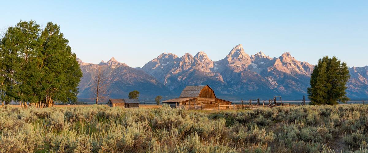 A wooden barn in a field with mountains in the background.