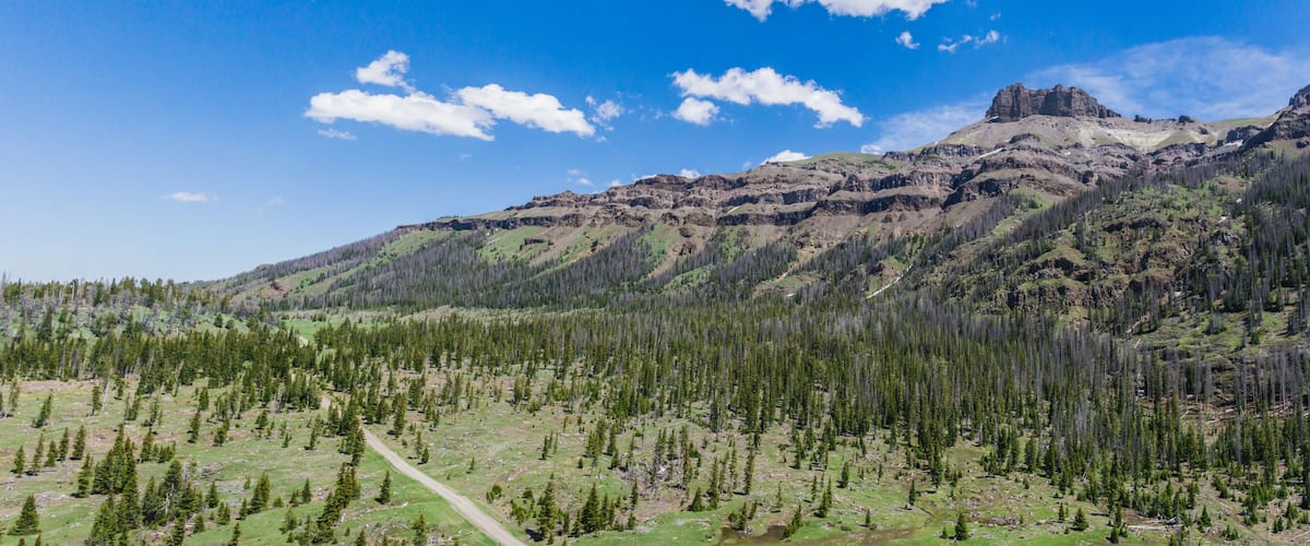 Un paysage montagneux caractérisé par un ciel dégagé, un sommet rocheux imposant et une vallée boisée.