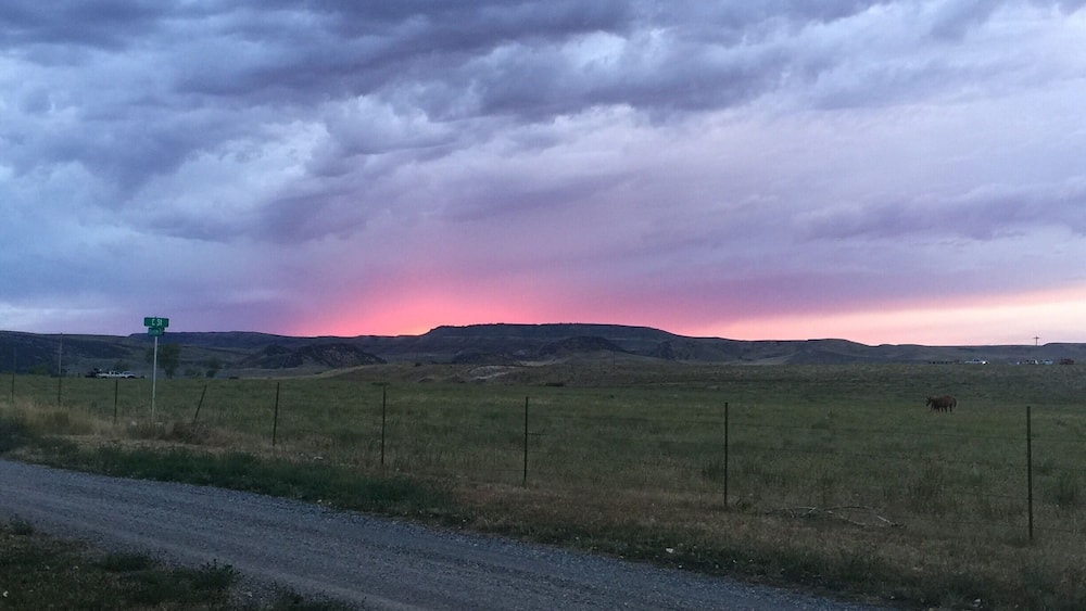 A rural landscape with a dirt road, a green signpost, and a sunset over rolling hills.