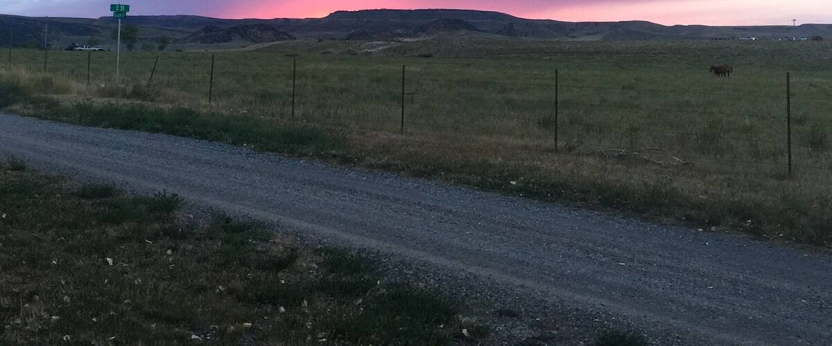 A rural landscape with a dirt road, a green signpost, and a sunset over rolling hills.