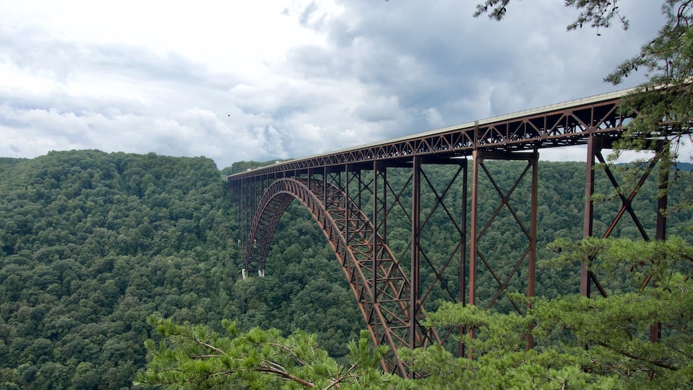 Un grand pont d’acier enjambant un profond ravin, avec en arrière-plan des collines densément boisées.