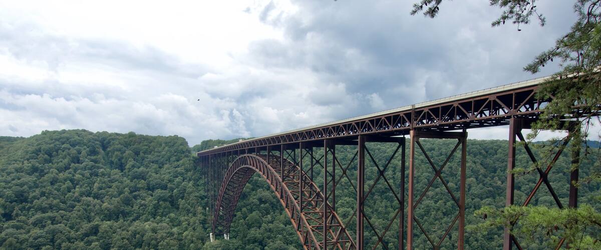 A large steel bridge spanning a deep gorge with dense forested hills in the background.