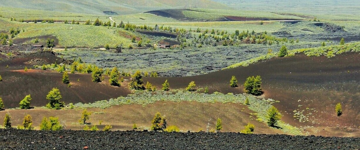 This is Craters of the Moon from the view atop Inferno Cone. A lot of contrast going on here with life springing from the ashes of lava tubes and spatter cones all atop a series of caves and tunnels to explore.
 I'd say go before July or the heat reflecting off the Obsidian may be too much to handle. If you come after that... run to the caves where it will be 15 - 20 degrees cooler.
Ooh, one last tip if you're camping in the campground try to get site #13. It's super private and makes you feel like you're in a crater. Otherwise try to book the group site as it's the only one that will allow a proper fire. :)