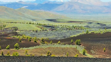 A mountainous landscape with green valleys, scattered trees, and distant snow-capped peaks.
