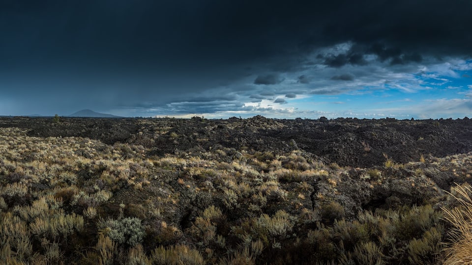 A rugged landscape with a mountain range in the distance, a road leading through the terrain, and a stormy sky.