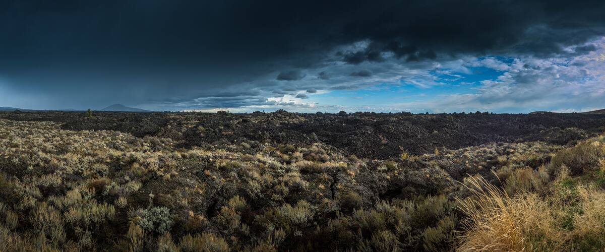A rugged landscape with a mountain range in the distance, a road leading through the terrain, and a stormy sky.