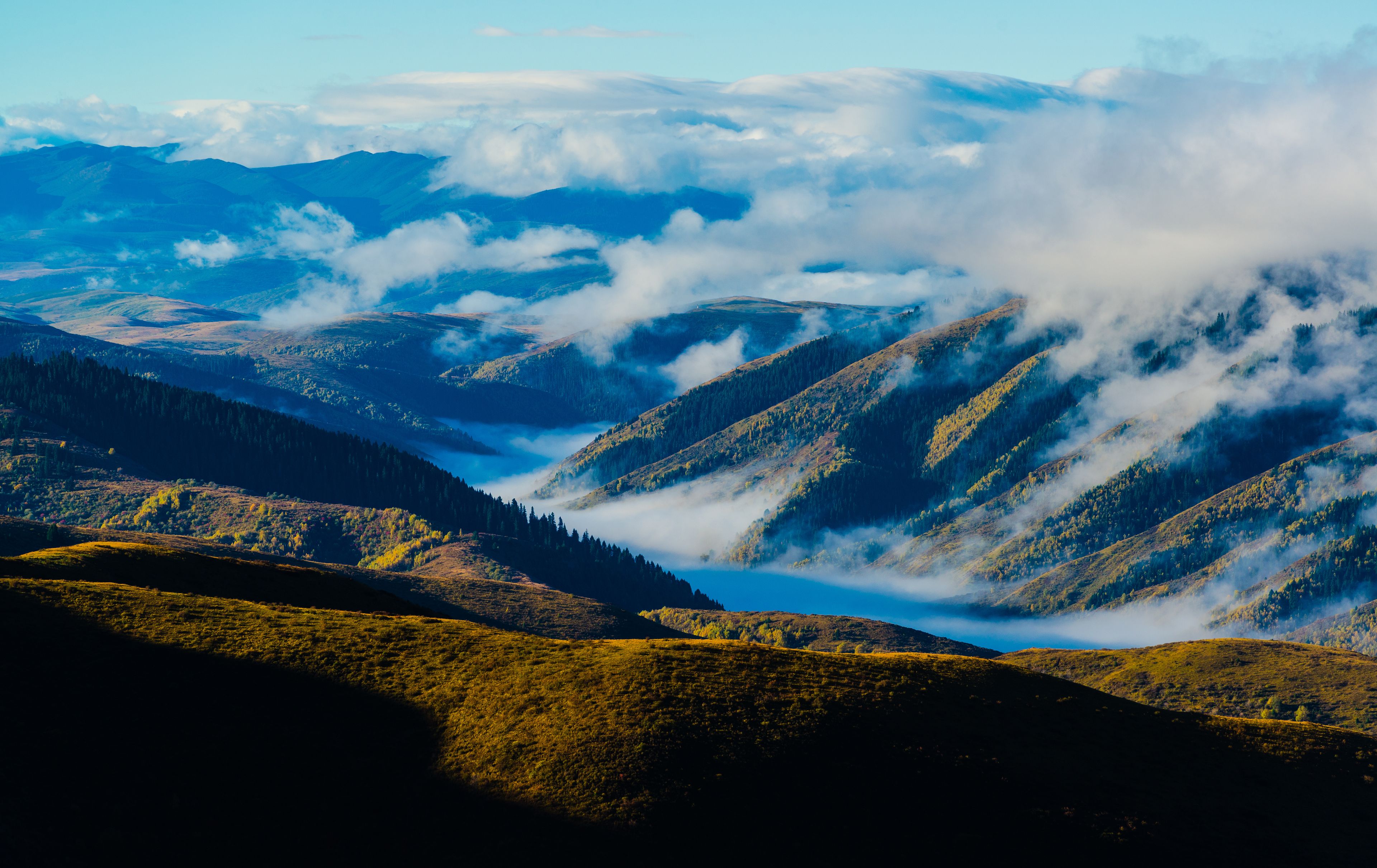 Eine gebirgige Landschaft mit Tälern und einem See, umgeben von bewaldeten Hügeln.