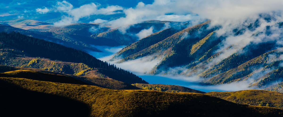 Eine gebirgige Landschaft mit Tälern und einem See, umgeben von bewaldeten Hügeln.