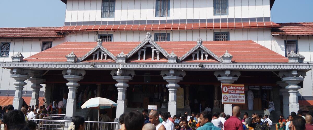 A large, traditional building with a red roof and white walls, featuring ornate architectural details and a crowd of people in front.