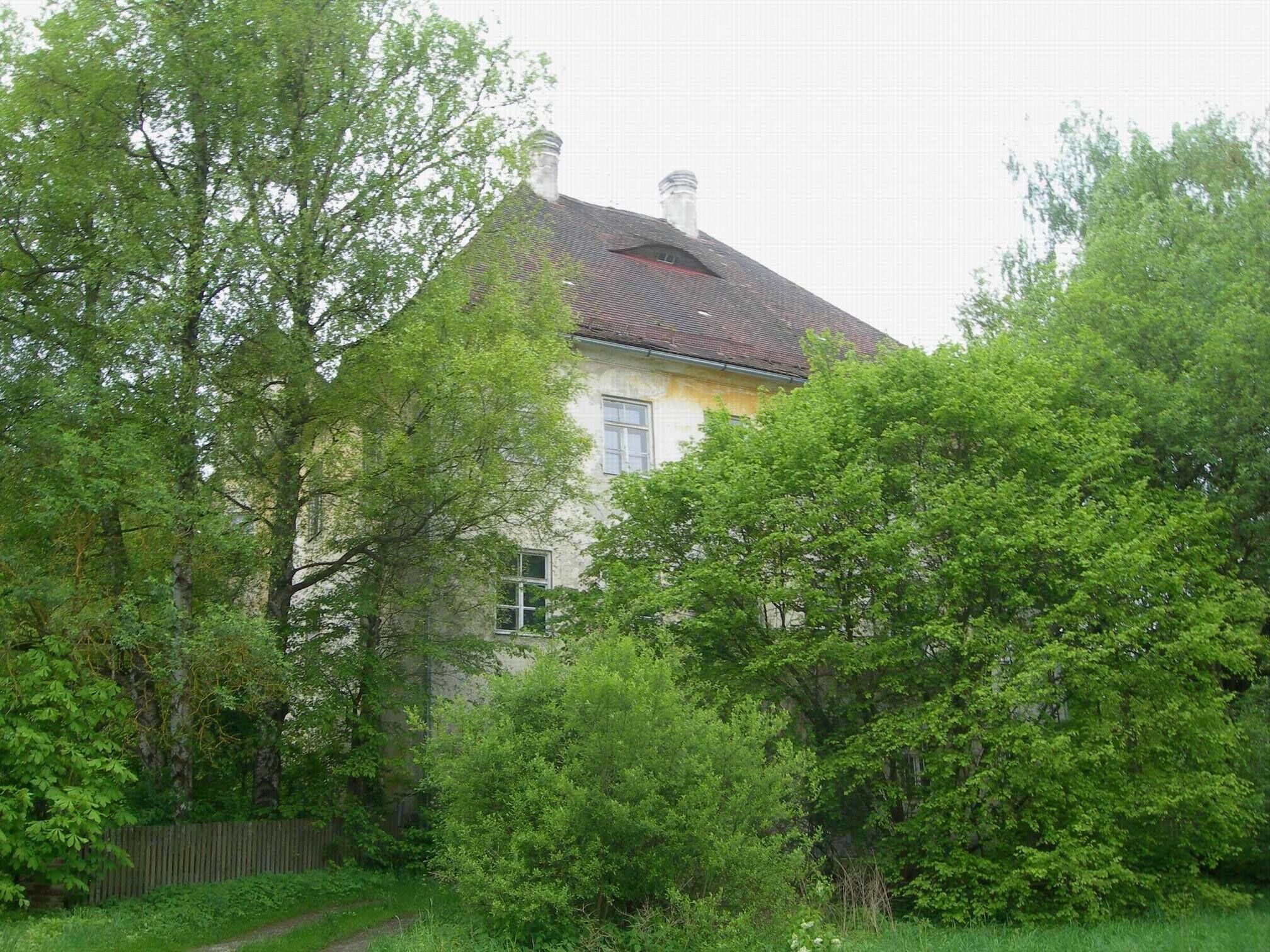 A house with a red roof, surrounded by lush green trees and a wooden fence.