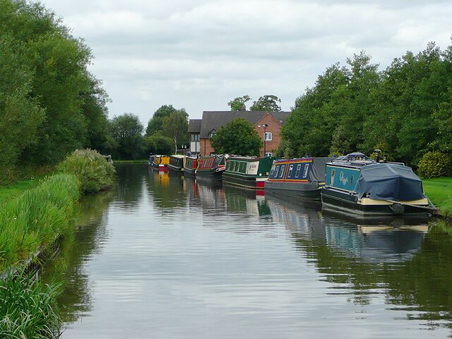 A canal with boats, greenery, and a house in the background.