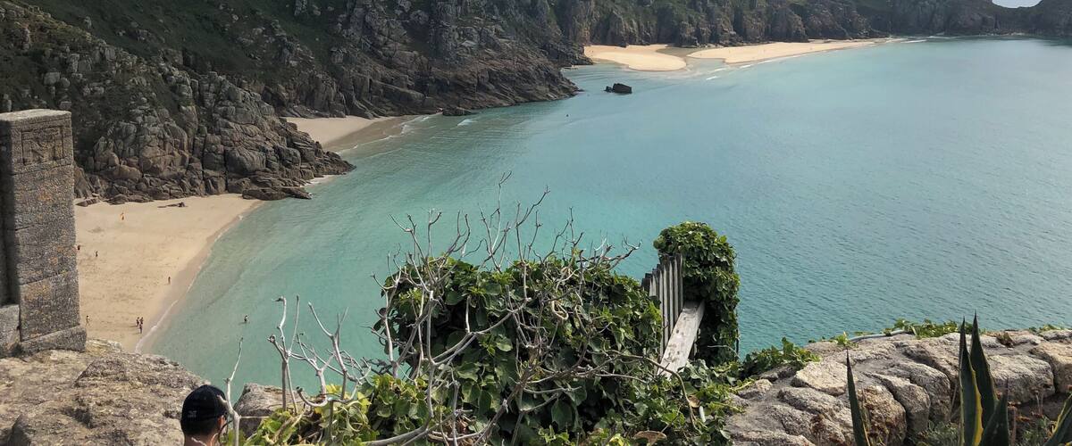 A coastal landscape with a sandy beach, rocky cliffs, and clear turquoise waters.