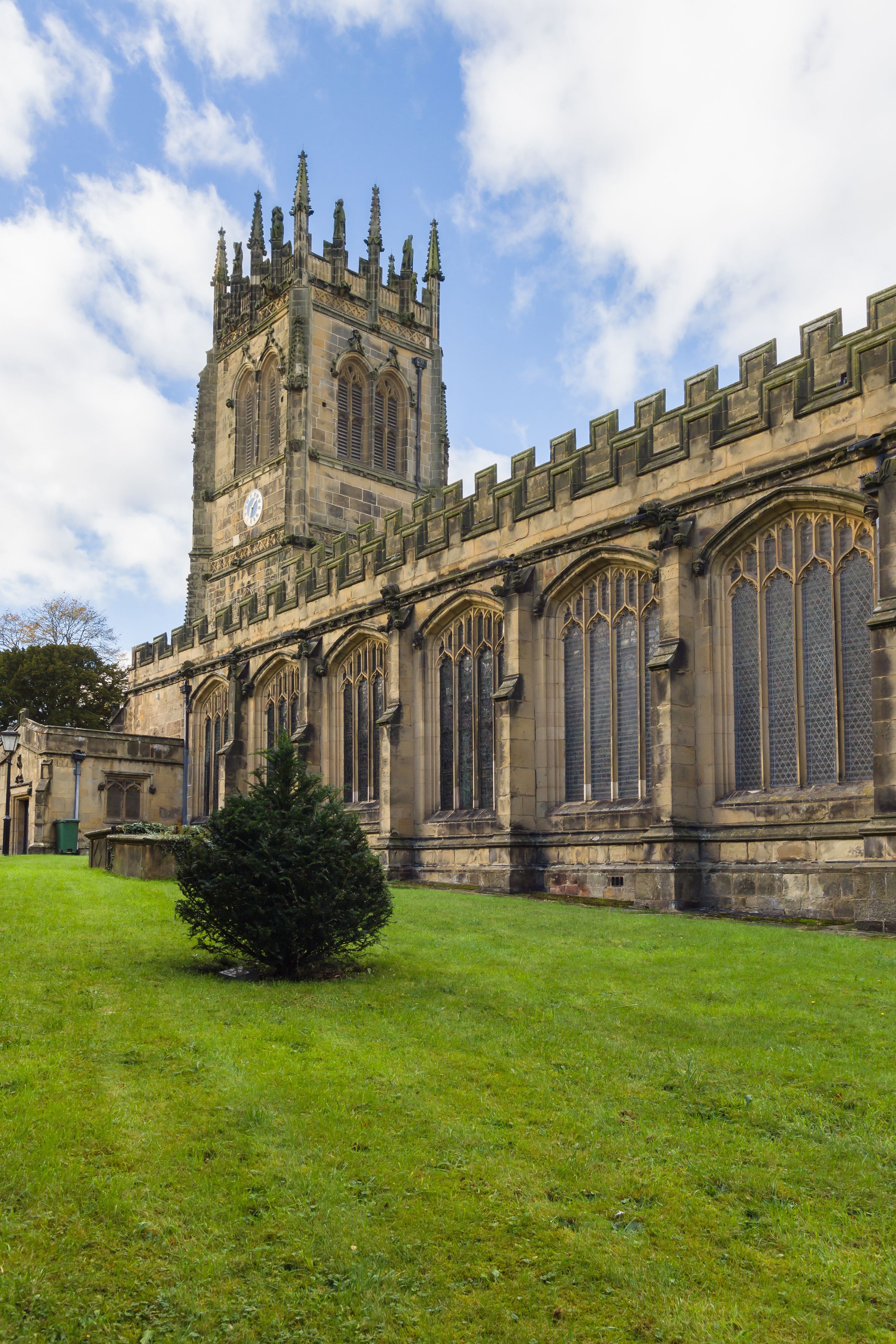 A historic building with a clock tower, large arched windows, and a well-maintained lawn.
