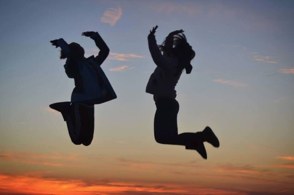 Two silhouetted figures jumping against a sunset sky.
