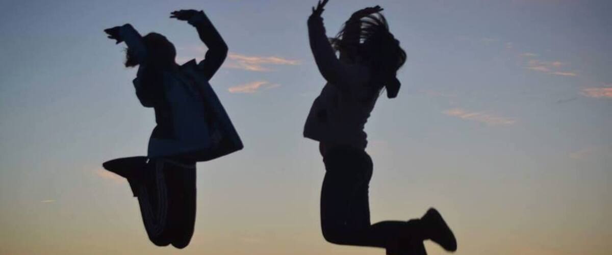 Two silhouetted figures jumping against a sunset sky.