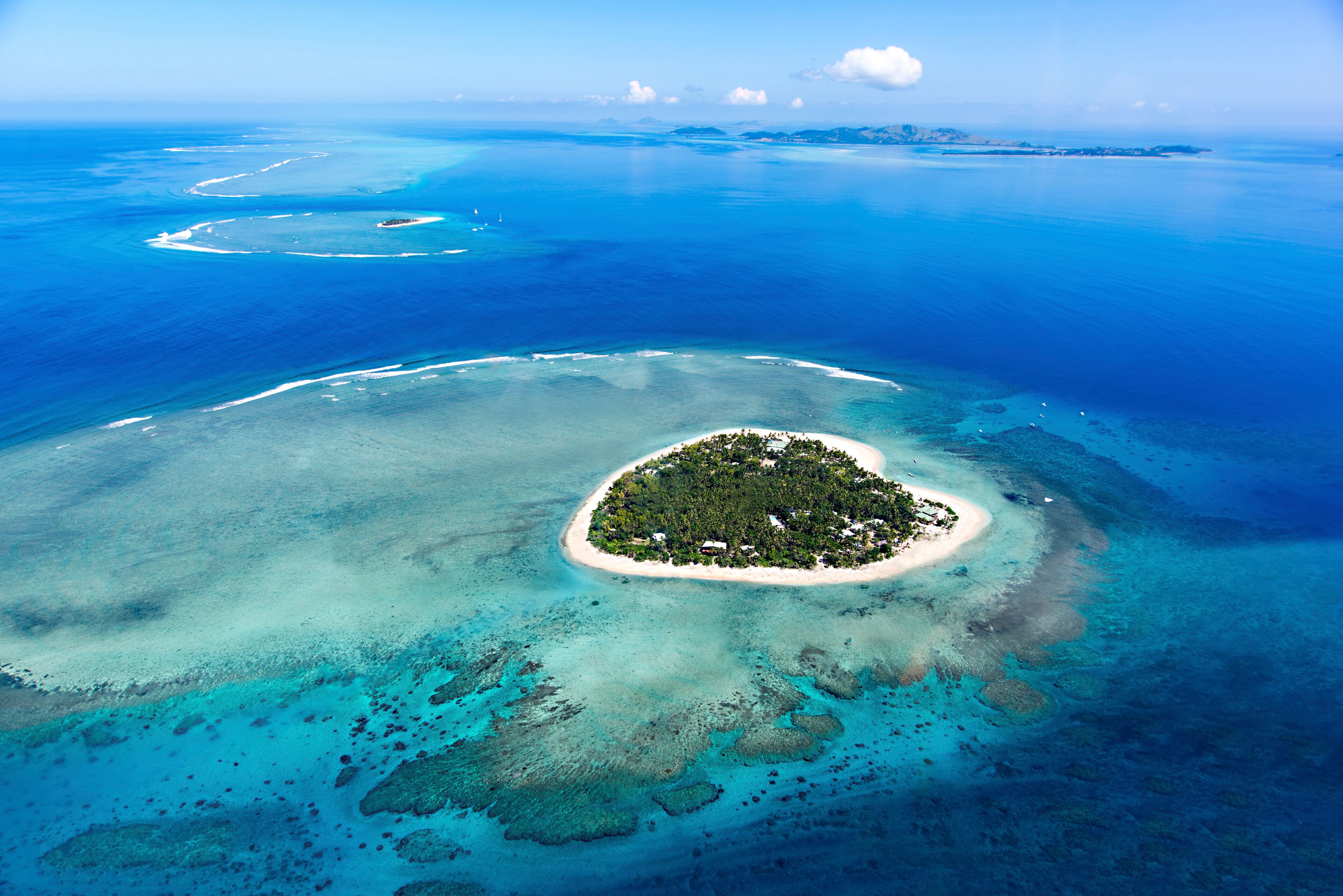An aerial view of a turquoise island surrounded by clear blue waters with coral reefs.