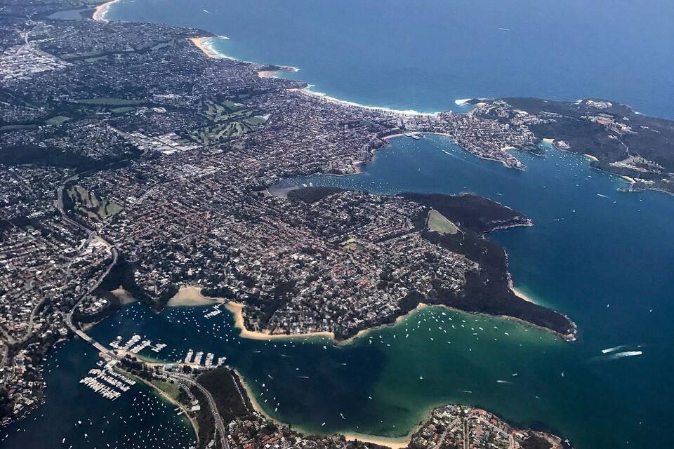 An aerial view of a coastal city with a dense urban area, a large bay, and a beach.
