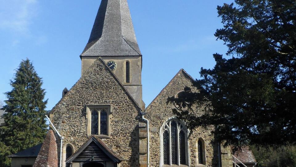 A stone church with a tall spire, a stone fence, and a graveyard.