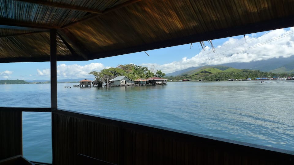A view of a calm lake with floating houses and a mountainous landscape in the background.