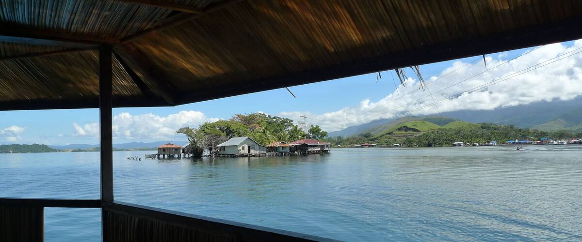 A view of a calm lake with floating houses and a mountainous landscape in the background.