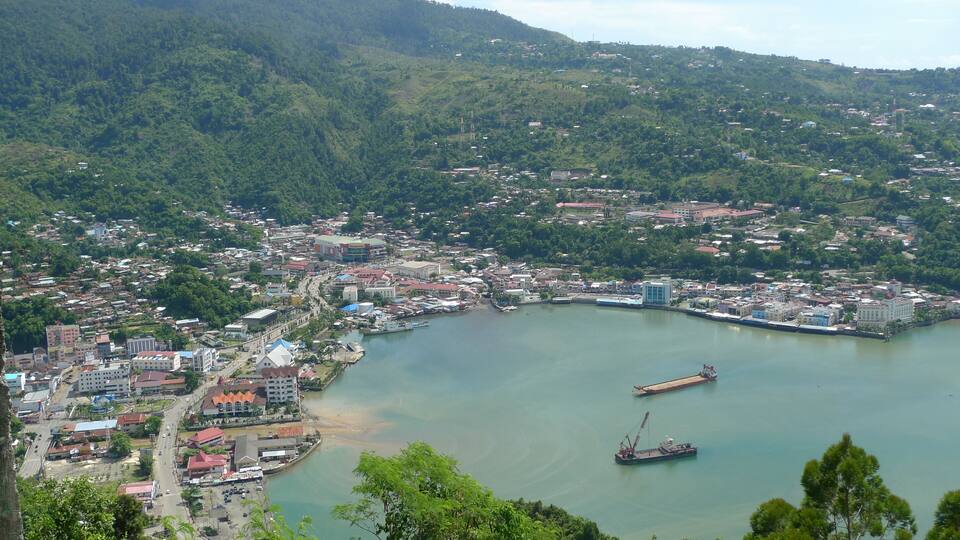 A coastal city with a bay, surrounded by hills and dense greenery.