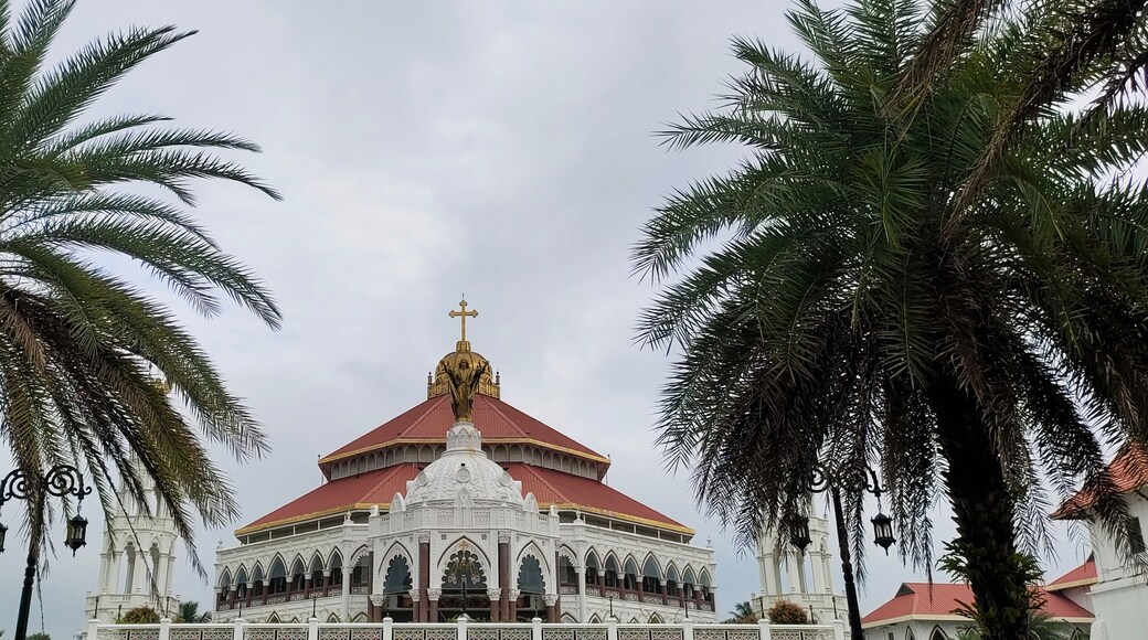 Famous and largest asian christian religion catholic church, chapel, cathedral, forane or shrine beautiful pilgrimage architecture building exterior in kerala india with palm trees and sky background.