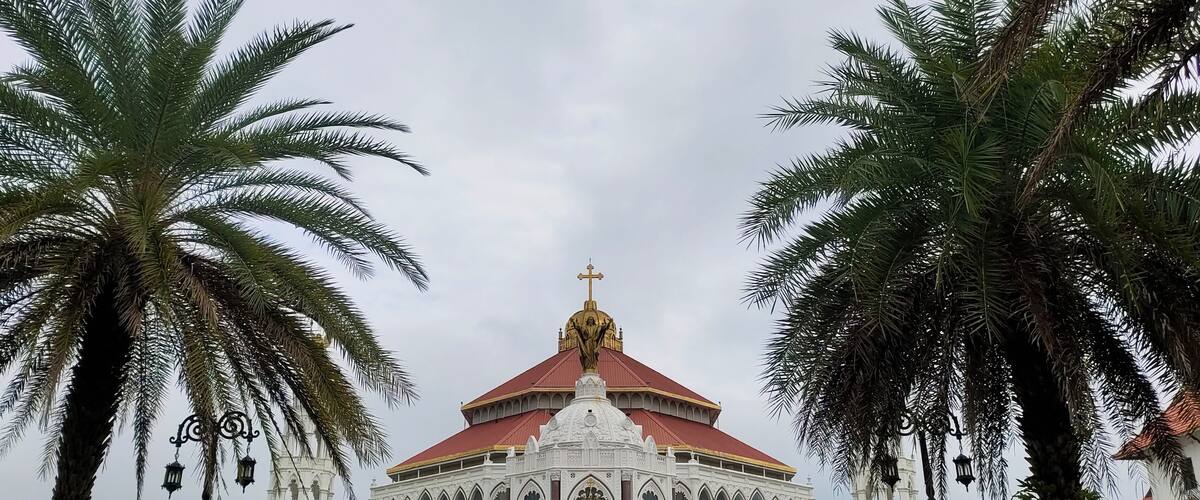 Famous and largest asian christian religion catholic church, chapel, cathedral, forane or shrine beautiful pilgrimage architecture building exterior in kerala india with palm trees and sky background.