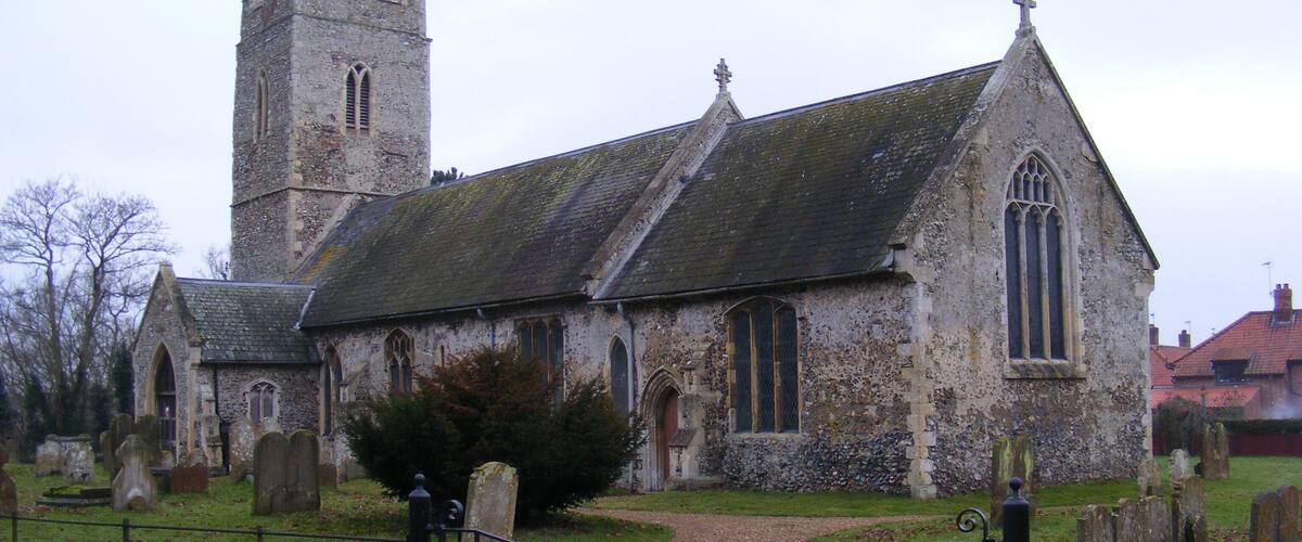 A historic church with a tall tower and a smaller steeple, surrounded by a cemetery with headstones.