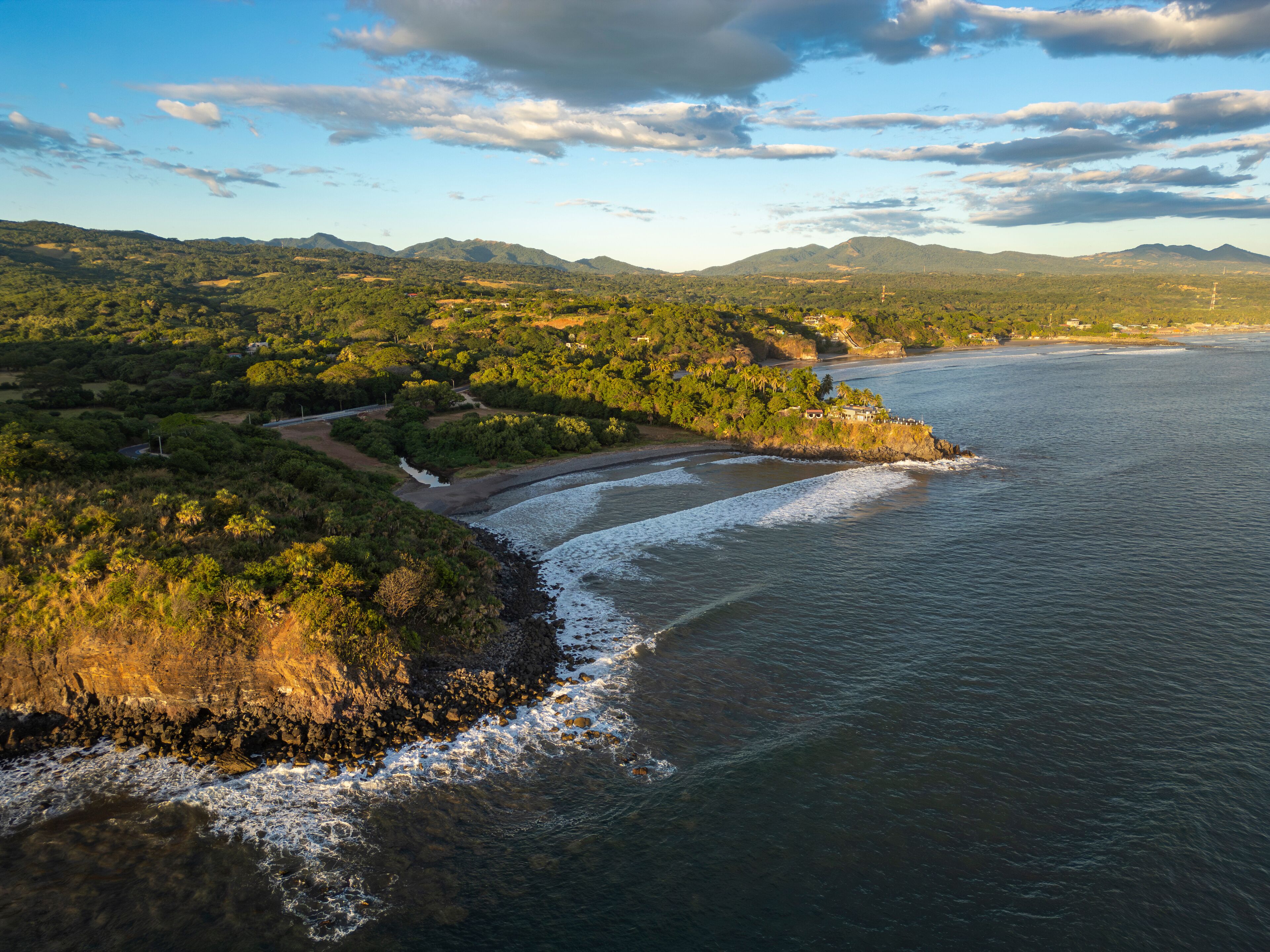 Aerial drone photo of the Pacific Ocean coast cliffs and lush green mountains, high waves. Sunny day, blue sky. El Cuco beach, El Salvador, Central America. South destinations travel concept.