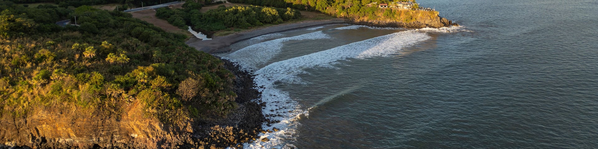 Aerial drone photo of the Pacific Ocean coast cliffs and lush green mountains, high waves. Sunny day, blue sky. El Cuco beach, El Salvador, Central America. South destinations travel concept.