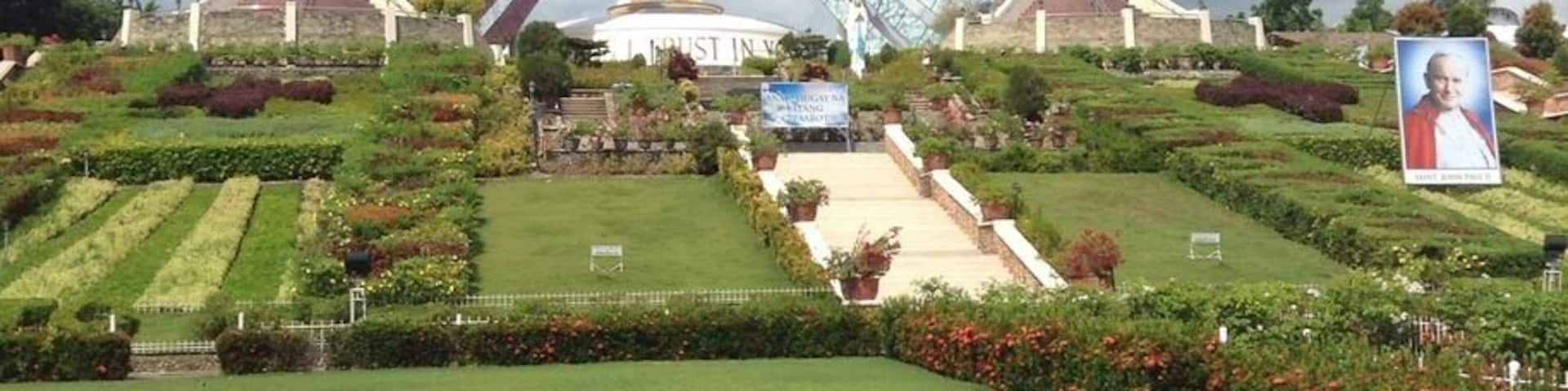 A large Ferris wheel with a white and red structure, surrounded by well-maintained gardens and a cloudy sky.
