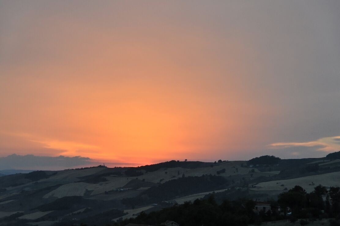A sunset over rolling hills with a clear sky.