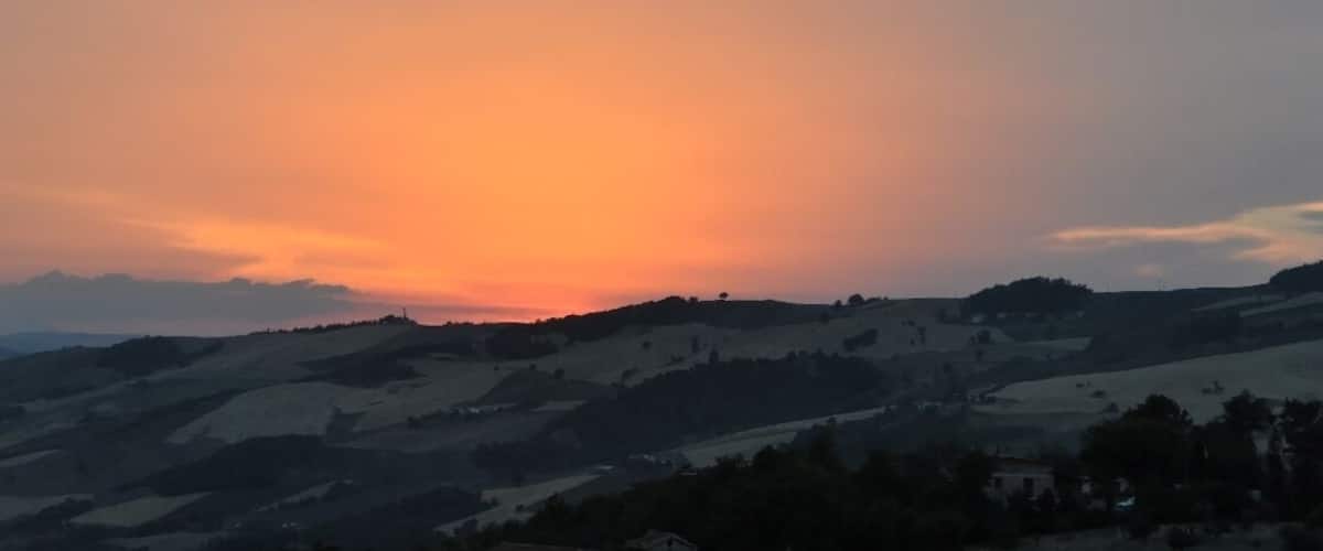 A sunset over rolling hills with a clear sky.