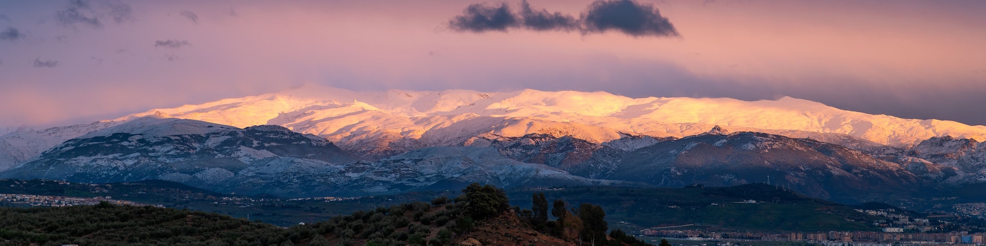 Una cordillera nevada al atardecer con un pueblo en el valle.