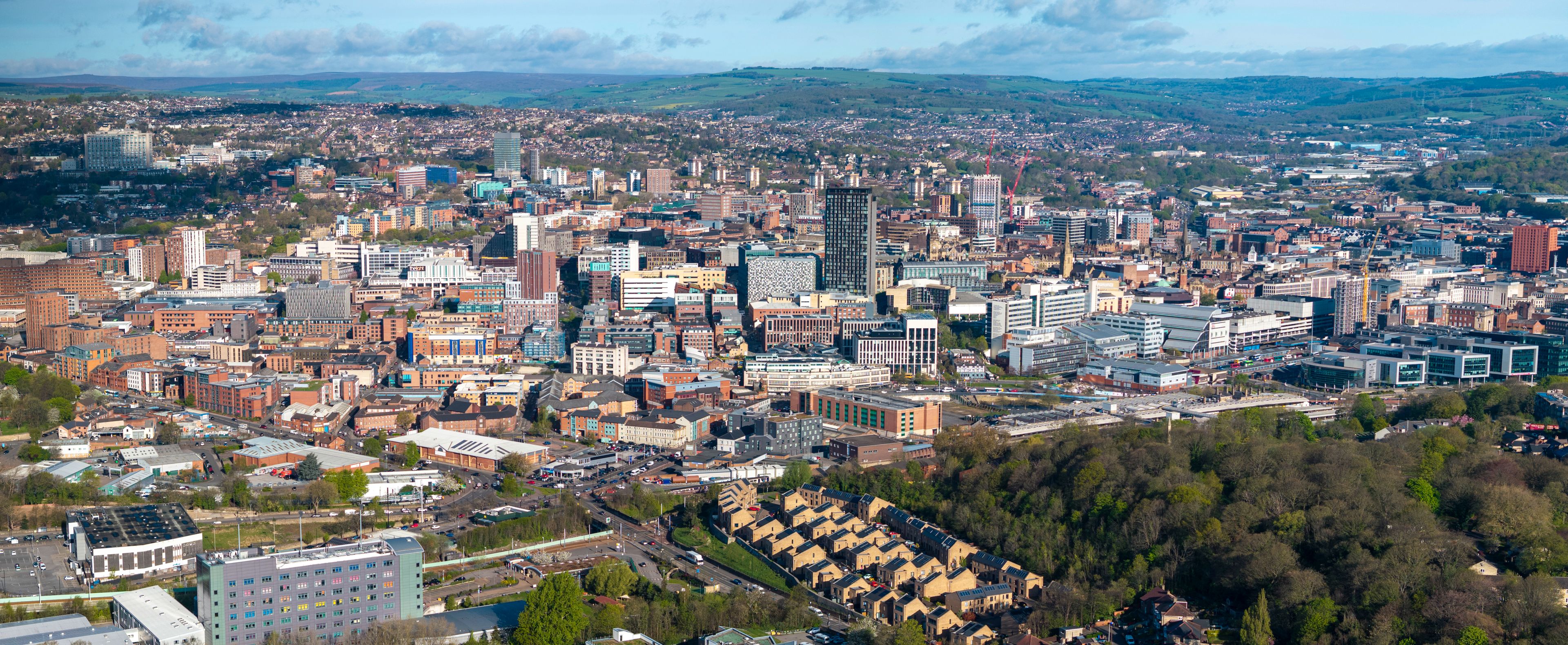 A cityscape with a mix of modern and older buildings, a river, and surrounding hills.