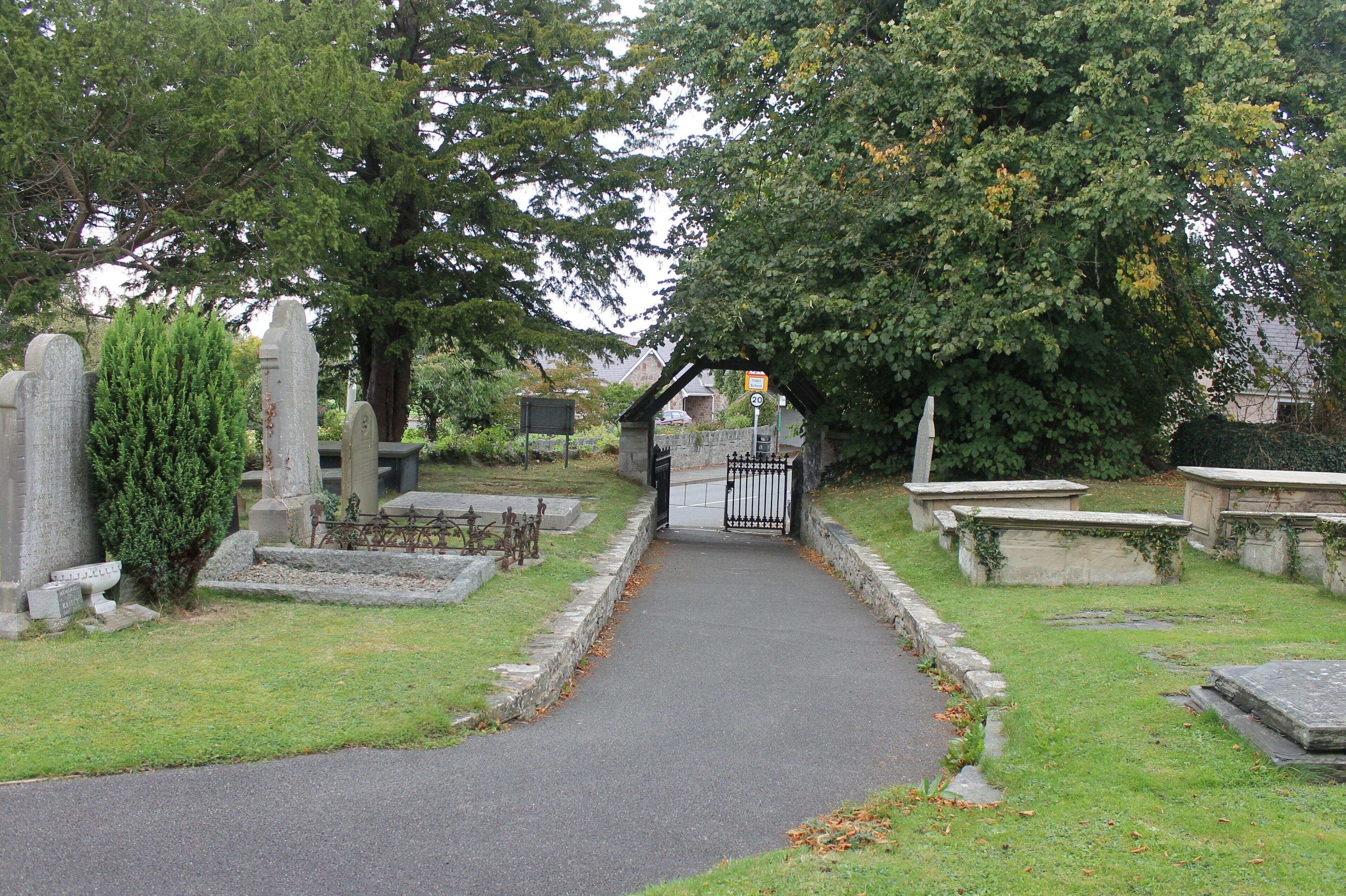 A cemetery with headstones, a paved path, and a gate.